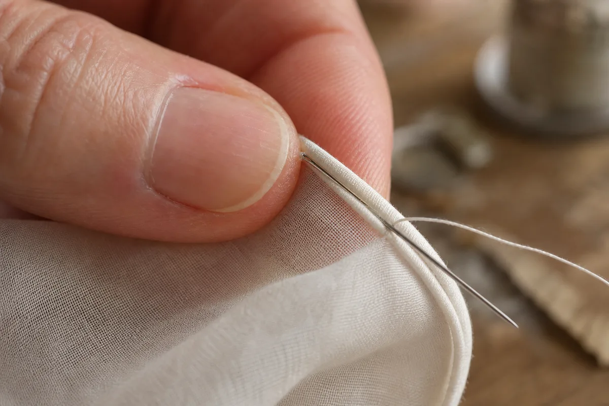 Détail d’un ourlet roulotté cousu à la main sur un tissu fin, fin bourrelet de tissu roulé entre les doigts